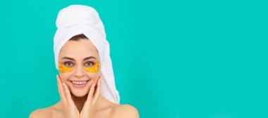 cheerful young lady has collagen golden eye patches on face with towel. Beautiful woman isolated face portrait, banner with mock up copy space