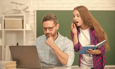 amazed father and child study at school with book and laptop on blackboard background, schoolwork.