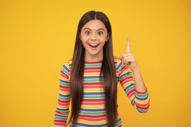 Mutlu yüz, pozitif ve gülümseyen genç kız duyguları. Sarı arka planda izole edilmiş, parmağıyla işaret eden genç bir kızın portresi. Kızın harika yeni bir fikri var. Başarılı çocuk.