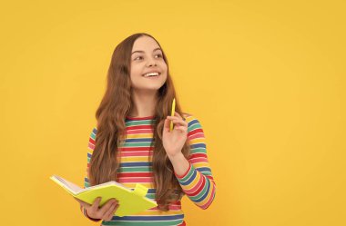 Zeka pırıltısı. Mutlu kızın elinde kalem tutan bir defter var. Dahi çocuk sarı arka plan. Okul eğitimi. Bir fikir yazıyorum..