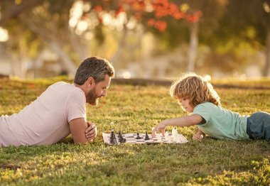 strategic and tactic. tutorship. dad and kid play logic game. father and son playing chess relaxing in park. fathers day. happy family. parenthood and childhood. checkmate. spending time together.
