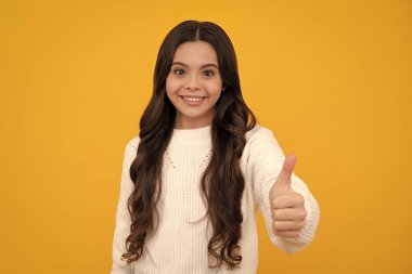 Mutlu yüz, pozitif ve gülümseyen genç kız duyguları. On iki, on üç, on dört yaşındaki ergen kız baş parmak hareketi yapıyor. Neşeli genç kız, sarı üzerine izole edilmiş, işaret veriyor.
