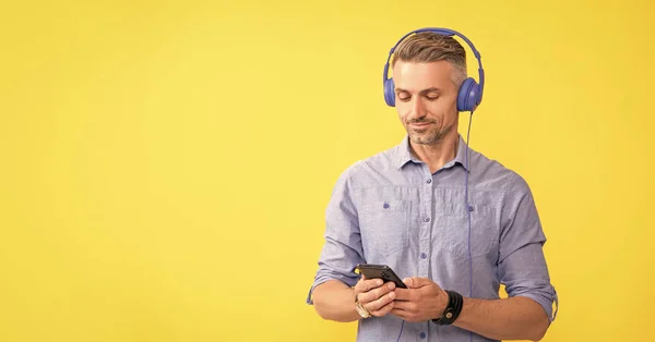 guy in headphones use smartphone. man listen music and hold phone. modern life and lifestyle. guy chatting in earphones. musical playlist. mobile music application. new app. copy space.