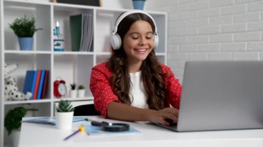 happy kid typing on laptop at online school lesson in earphones, modern life.