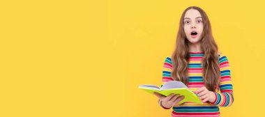 Surprised open-eyed kid hold school book yellow background, surprise. Portrait of schoolgirl student, studio banner header. School child face, copyspace