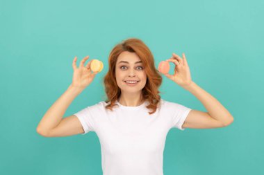 surprised lady hold sweet macaron french cookie on blue background.