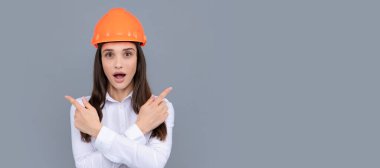 Woman isolated face portrait, banner with mock up copy space. Architect woman wearing helmet over gray background, pointing finger