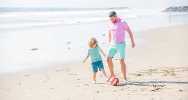 dad and child having fun outdoors. childhood and parenting. family holidays. sport activity. funny father and son play football on beach. daddy with kid boy on summer day. weekend family day.