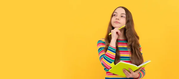 Thoughtful girl child think holding school copybook and pen yellow background, thinking. Banner of schoolgirl student. School child pupil portrait with copy space