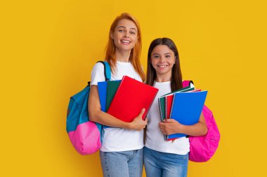 Okul çantalı ve kitap okumaya hazır anne-kız okul kızları. Okula dönelim. Anne ve çocuk izole edilmiş sarı stüdyo geçmişinde