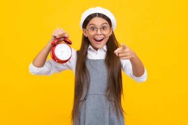 Child student girl with clock isolated on yellow background. Child back to school. Education and time concept. Excited face, cheerful emotions of teenager girl