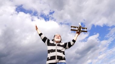 Happy elderly man pretend flying on toy airplane in sky, journey.