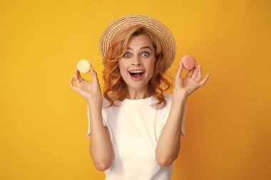 Tatlı, genç bir kadın. Kurabiye tutuyor. Güzel gülümseyen genç kız sarı arka planda renkli badem kurabiyeleri yiyor.