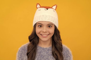 Sarı arka planda süveter ve şapka giyen mutlu çocuk, kış.