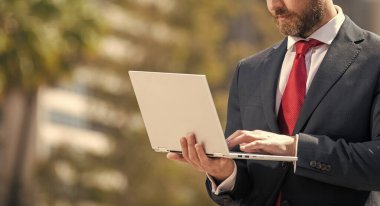confident man in elegant suit typing on pc outside, copy space, networking.