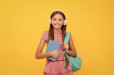 Mutlu çocukluk. Okul çantalı çocuk. Müzik. Mutlu genç kız sırt çantası taşıyor. Okula dönüyorum. Bilgi günü. Eğitim konsepti. Sarı arka planda çalışma kitabı olan kulaklıklı çocuk. Eylül 1.