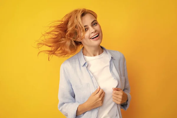 Redhead woman with movement hair. Studio shot of carefree redhead woman smiles cheerfully isolated over vivid yellow background in good mood