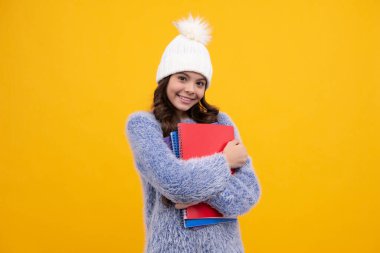 Portrait of school teenage girls in autumn hat holding copybooks and backpack over yellow background. Autumn school. Happy schoolgirl, positive and smiling emotions