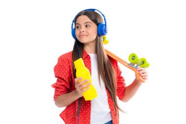 Teen girl 12, 13, 14 years old with skateboard water bottle and headphones over studio background. Cool modern teenager in stylish clothes. Teenagers lifestyle, casual youth culture