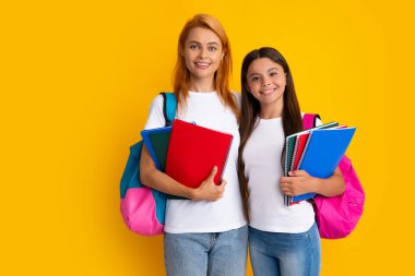 Okul, öğrenme ve eğitim konsepti. Okul çantalı ve kitapları öğrenmeye hazır anne-kız okul kızları. Okula dönelim. Anne ve çocuk izole edilmiş sarı stüdyo geçmişinde