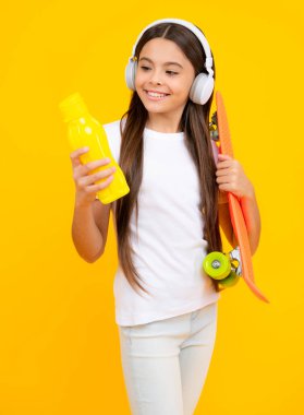 Mutlu ergen portresi. Gençlik gündelik kültürü. Stüdyonun arka planında kaykay ve kulaklıkları olan genç bir kız. Moda tarzında giyinmiş bir genç. Gülümseyen kız