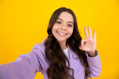 Summer teen girl making selfie posing on yellow background. Fashion teenager, casual look. Happy teenager, positive and smiling emotions of teen girl