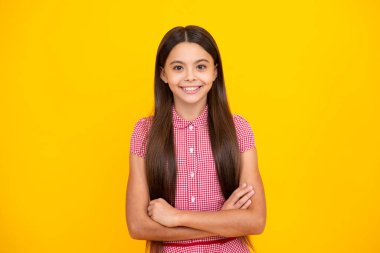 Sevimli küçük kız sarı arka planda kollarını kavuşturuyor.