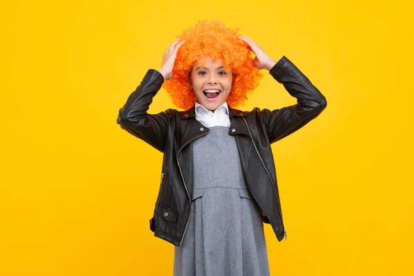 Beautiful teenage girl in wig isolated on yellow. Funny clown wig. Excited face, cheerful emotions of teenager girl