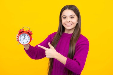 Portrait of teenage girl with clock alrm, time and deadline. Studio shot isolated on yellow background