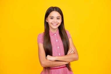 Teenage girl kid with crossed arms, looking at camera, isolated on yellow studio background
