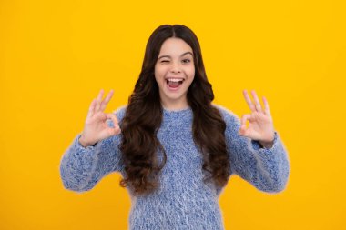 Funny teen child over yellow background doing ok gesture and winking with hand smiling with happy face. Amazed teenager. Excited teen girl