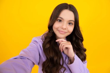 Ergen yaşam tarzı. Süslü takım elbiseli güzel bir kız çocuğu sarı arka planda pozitifleştirilmiş selfie yapıyor. Mutlu ergen, pozitif ve gülümseyen genç kız duyguları