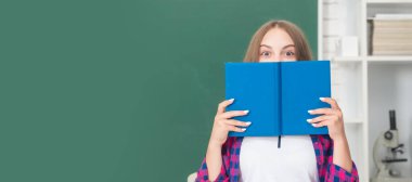 teen girl in high school behind workbook at blackboard. Portrait of schoolgirl student, studio banner header. School child face, copyspace