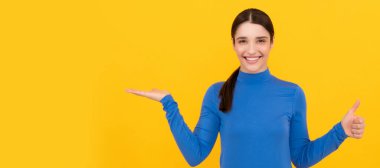 amazed woman portrait pointing fingers on copy space yellow background showing thumb up, emotions. Woman isolated face portrait, banner header poster with mockup copyspace