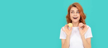 amazed girl hold sweet macaron french cookie on blue background. Woman isolated face portrait, banner with mock up copyspace