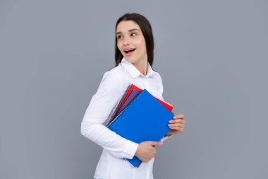 Teenager student girl isolated on grey background. Cheerful young woman student in shirt hold notebooks showing. High school university college students