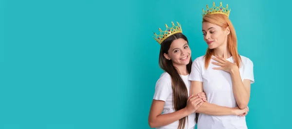Mother and daughter child banner, copy space, isolated background. Selfish woman mother smile at happy girl child in crowns blue background, daughter
