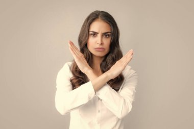 Negatif kadın ellerini çapraz yapmış. Gri arka planda izole edilmiş yasak bir kural yok. Memnun olmayan kızgın kadın teklifi engelliyor, çapraz duruş hareketi gösteriyor, olumsuz yanıt