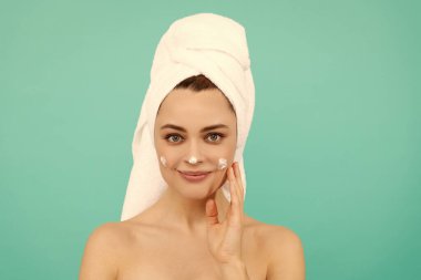 Gülümseyen genç bayan mavi arka plana yüz kremi sür..