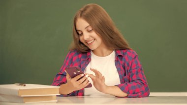 Mutlu çocuk akıllı telefondan konuşuyor. Sınıfta, tahtada, iletişimde..