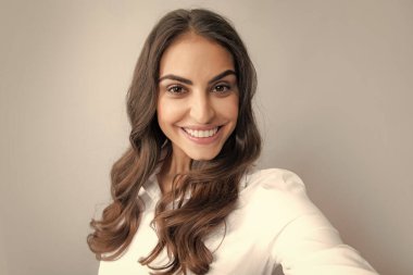 Gülümseyen neşeli kadın gri arka planda cep telefonuyla selfie çekiyor.