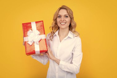 Neşeli kadın sarı arka planda büyük bir hediye kutusu tutuyor..