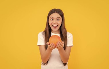 Şaşkın çocuk sarı arka planda greyfurt tutuyor, sağlık.