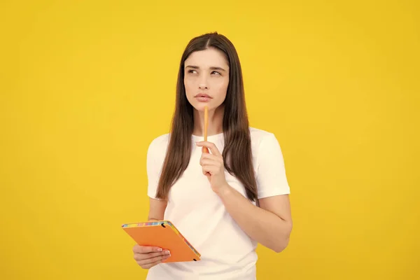 Thinking student. Portrait of student woman. College or high school ducation. Serious young woman with notebooks at camera on yellow studio background. Young female university student