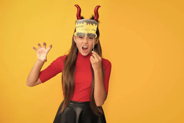 evil child in imp horns with party accessory. happy halloween. devil kid with pumpkin. trick or treat. teen girl show claws on yellow background. celebrate autumn holiday. childhood fun.