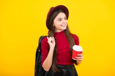 12, 13, 14 yaşlarındaki çocuk elinde bir fincan kapuçino ya da çay ile. Sarı arka planda yemek kupası olan ergen, sabah içeceği. Mutlu ergen portresi. Gülümseyen kız