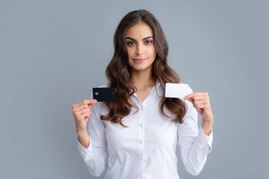 Gri arka planda kredi kartı tutan gömlekli güzel bir kadının portresi. Neşeli kız banka kartı çözümü gösteriyor
