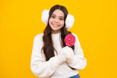 Şekerli lolipop yiyen genç bir kız. Çocuklar için şeker ve şeker. Çocuk, sarı izole arka planda lolipop dondurması yiyor. Lezzetli karamel, şekerci dükkanı. Mutlu gülümseyen kız