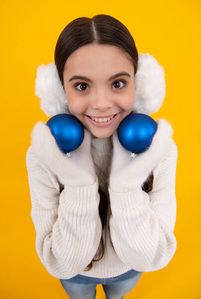 Happy kids face close up. Teenager child santa girl in fur sweater, christmas ball isolated on yellow background. Happy New Year, celebration holiday concept