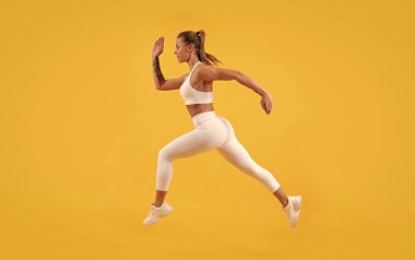 Sarı arkaplanda koşan aktif sporcu kız koşucu.
